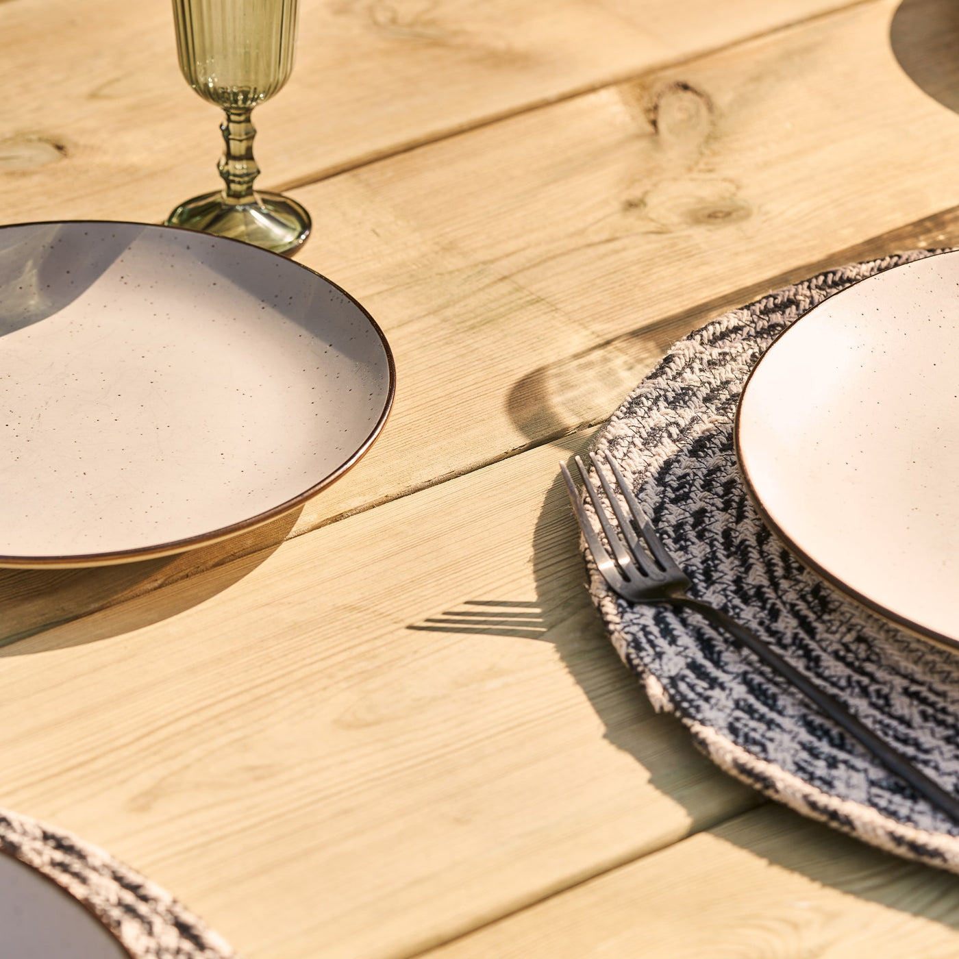 A close-up view of a chunky wooden table top set with plates, glasses and cutlery. This chunky rustic farmhouse style garden table is handcrafted from FSC-certified sustainable timber and features a bold 45mm thick tabletop.