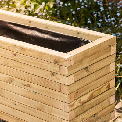 A corner view of a rectangular wooden garden planter. The durable timber planter has a modern, sleek design and is lined ready for planting.