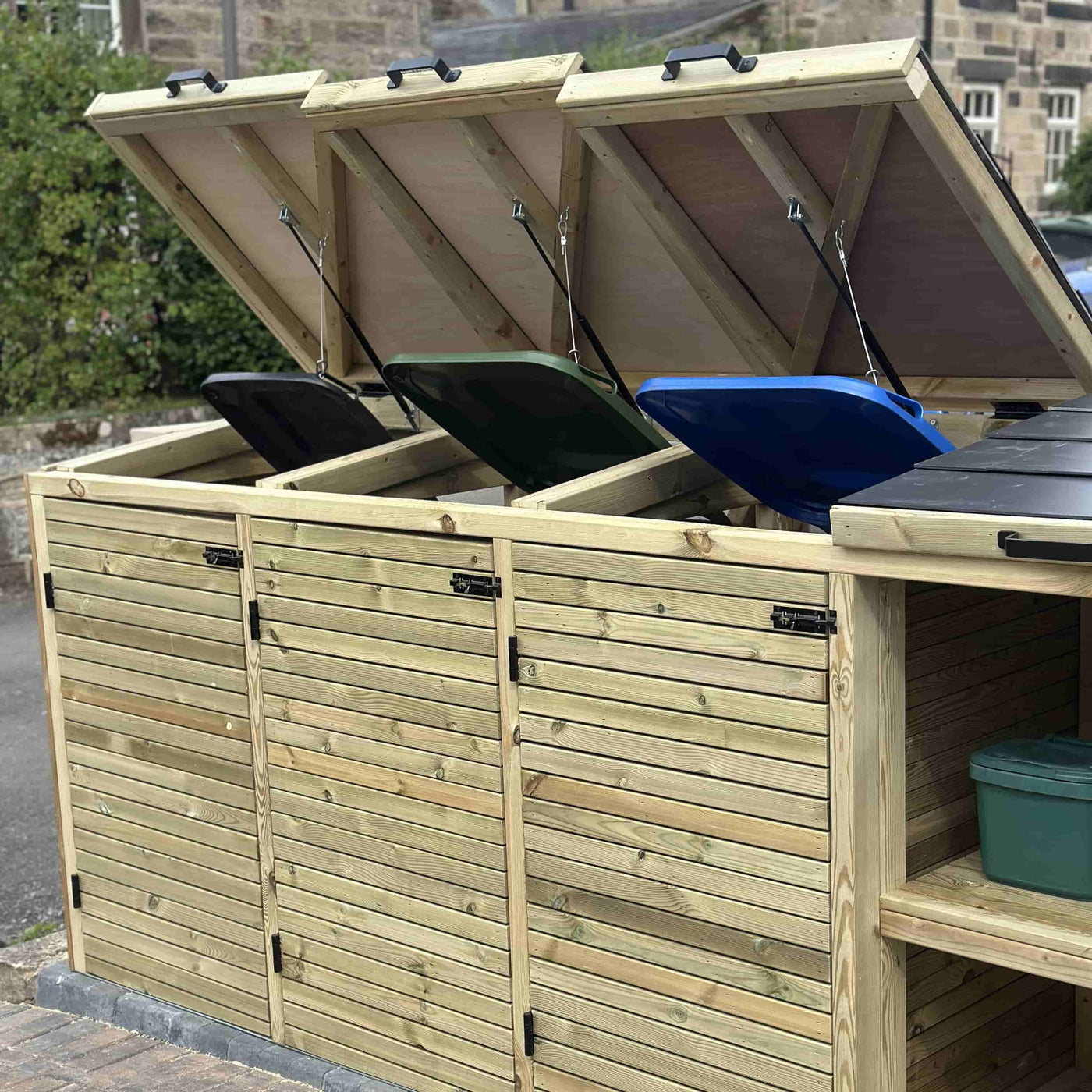 Wooden outdoor storage unit with open lids revealing wheelie bins. Triple wooden bin store with additional storage.