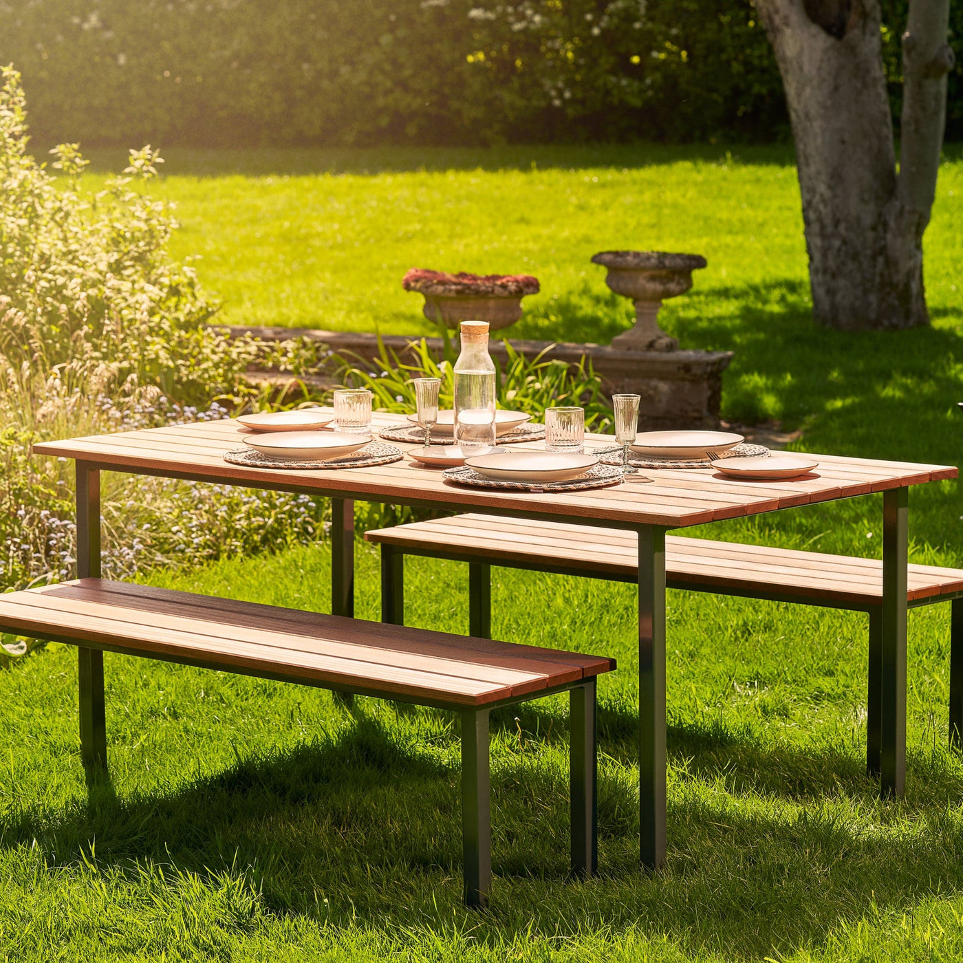 Hardwood Garden Table & Benches. The table is set with white plates and cutlery and sits of lush green grass. 