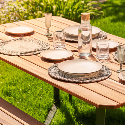 A top view of a Hardwood Outdoor Dining Set with an angled design. The table is set with plates, cutlery and glasses and sits on a lush garden lawn.