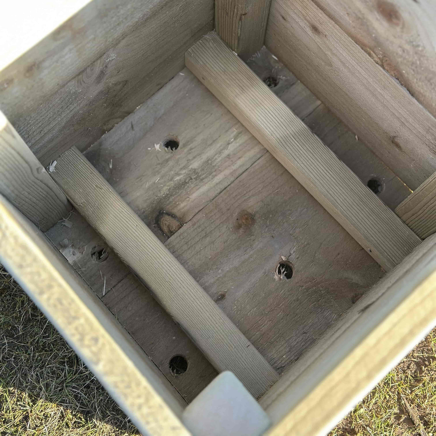 Inside view of a square wooden planter box, drainage holes are visable.