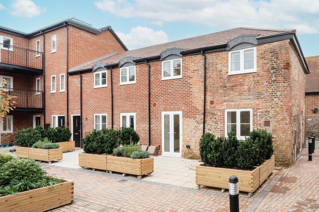 A modern housing courtyard filled with bespoke wooden planters on wheels, built by Timber Foundry. The planters are full of large green trees and plants.