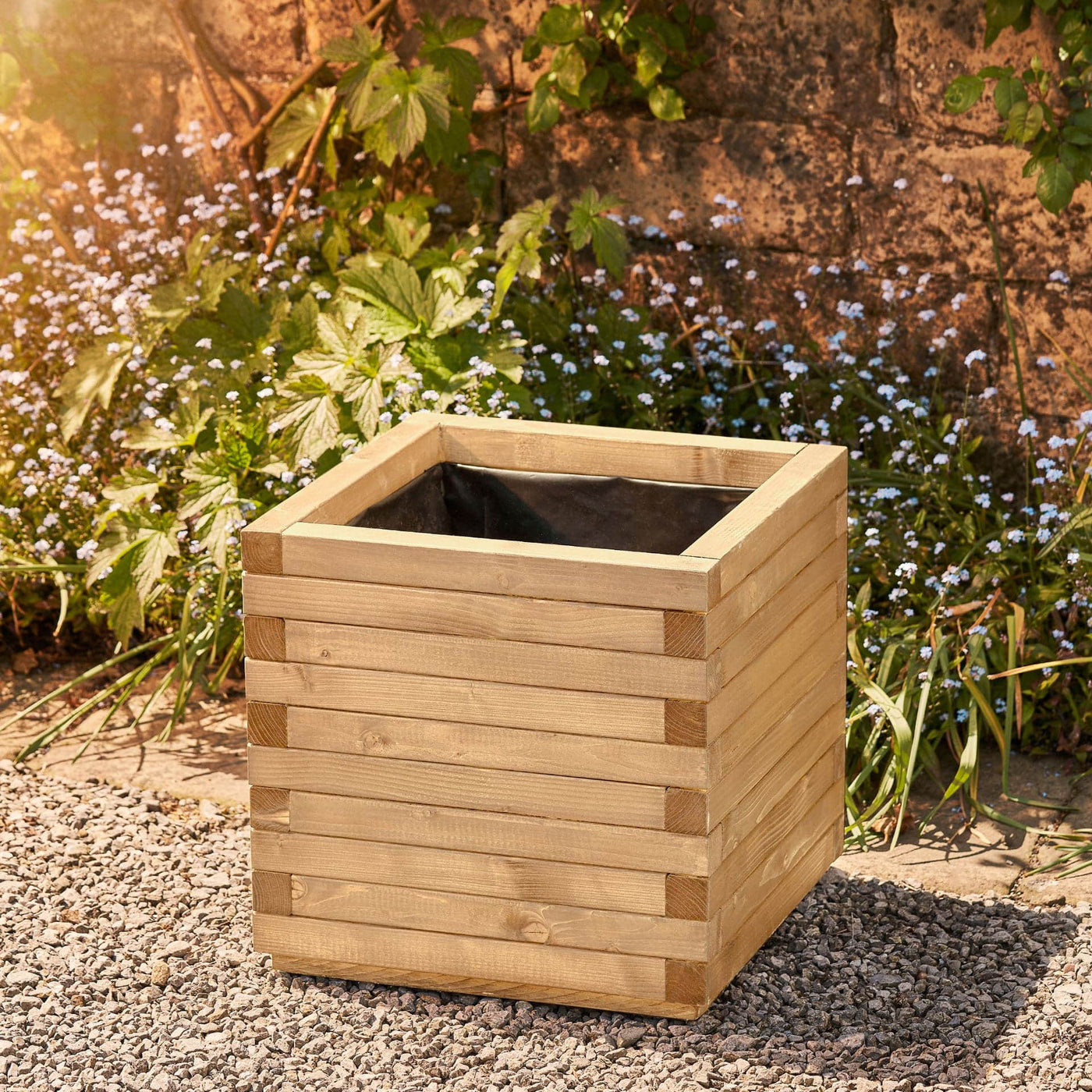 Large square wooden planter in a natural finish with a modern, sleek design. This durable planter is lined and ready for planting. Positioned against a wall with climbing green plants.