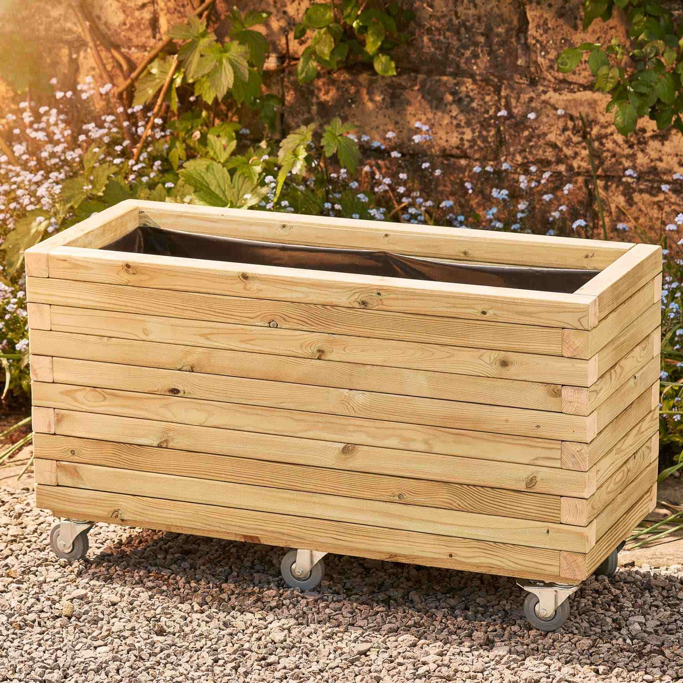 Large rectangular garden planter in a natural finish, lined for added functionality. This durable wooden planter features a modern, sleek design and is placed against a wall with climbing green plants.