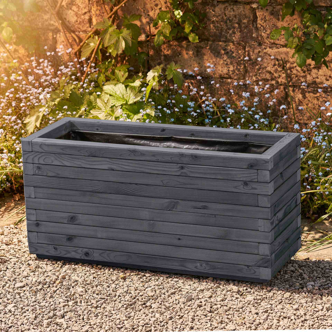 The Large rectangular garden planter has an ironstone grey finish and is lined for added functionality. This durable wooden planter features a modern, sleek design and is placed against a wall with climbing green plants.