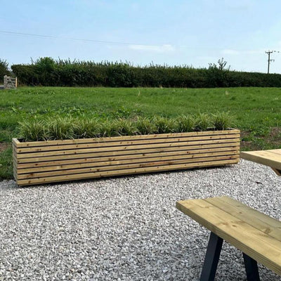 Long garden wooden planter, contemporary design. The large planter is filled with evergreens.