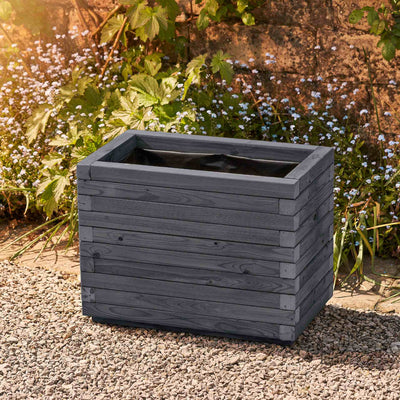 Medium rectangular garden planter in an ironstone grey finish, lined for added functionality. This durable wooden planter features a modern, sleek design and is placed against a wall with climbing green plants.