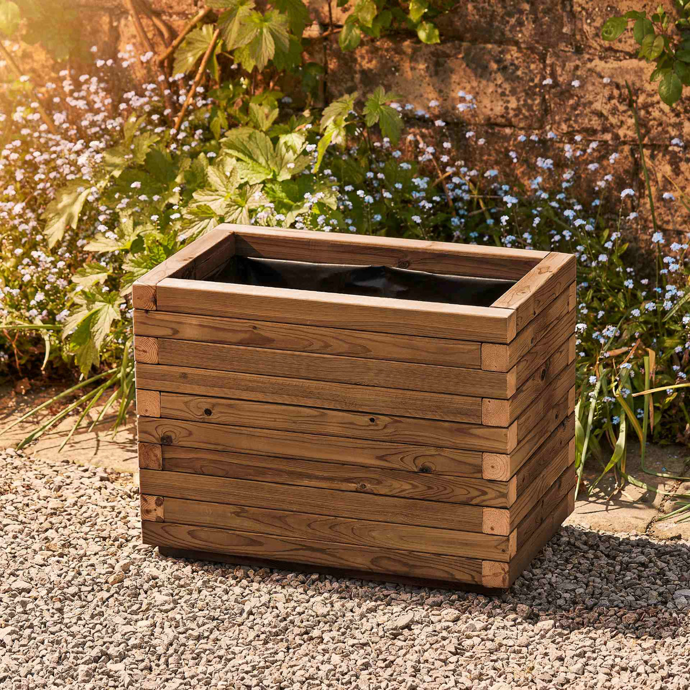 Medium rectangular garden planter in a medium oak finish, lined for added functionality. This durable wooden planter features a modern, sleek design and is placed against a wall with climbing green plants.