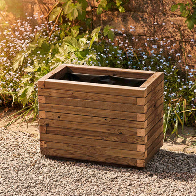 Medium rectangular garden planter in a medium oak finish, lined for added functionality. This durable wooden planter features a modern, sleek design and is placed against a wall with climbing green plants.