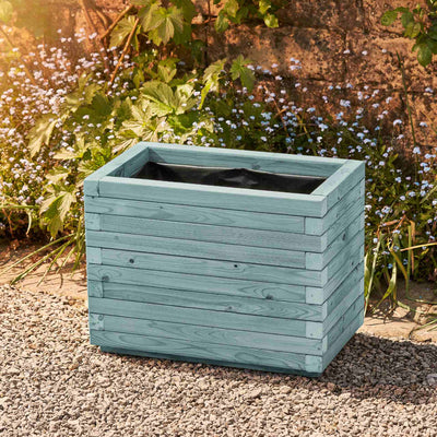 Medium rectangular garden planter in a beach hut blue finish, lined for added functionality. This durable wooden planter features a modern, sleek design and is placed against a wall with climbing green plants.