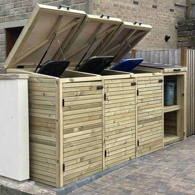 Wooden outdoor storage unit with hinged lids for trash cans against a brick wall.