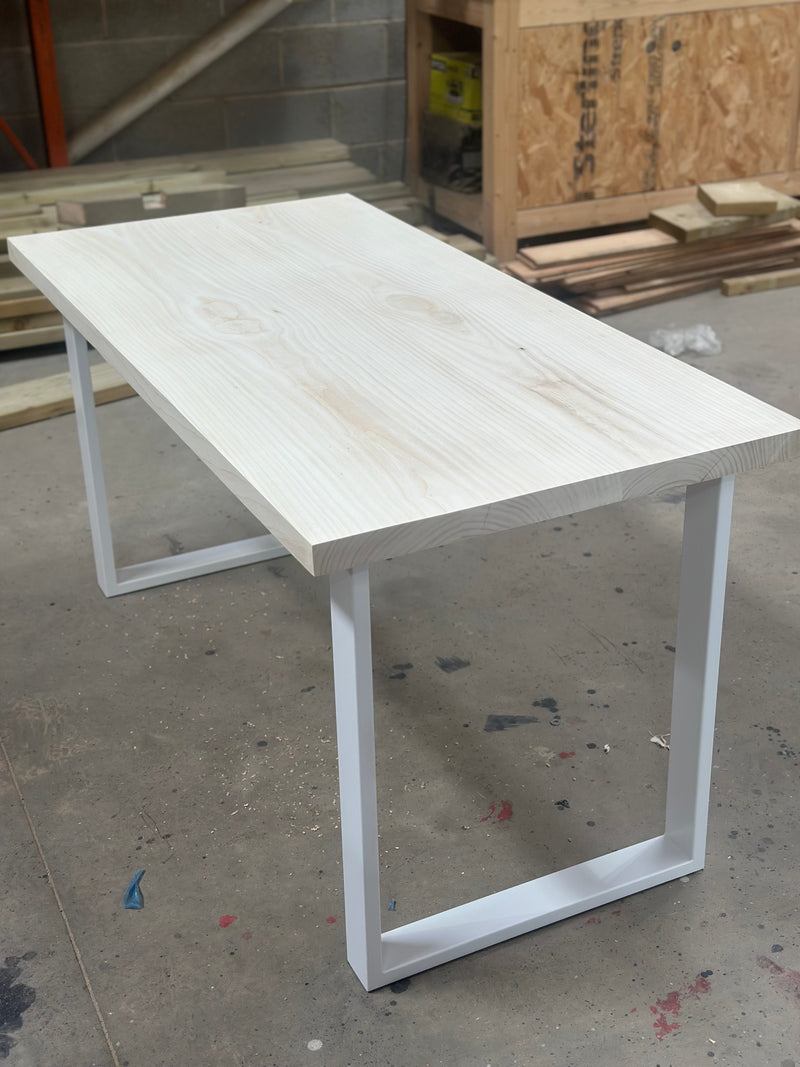 A finished bespoke English ash table on a white steel frame in the workshop, ready to leave