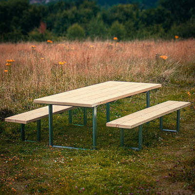A Rustic Wooden Garden Table with Steel Box Legs and matching benches. A scenic landscape with lush green trees surrounds the set.