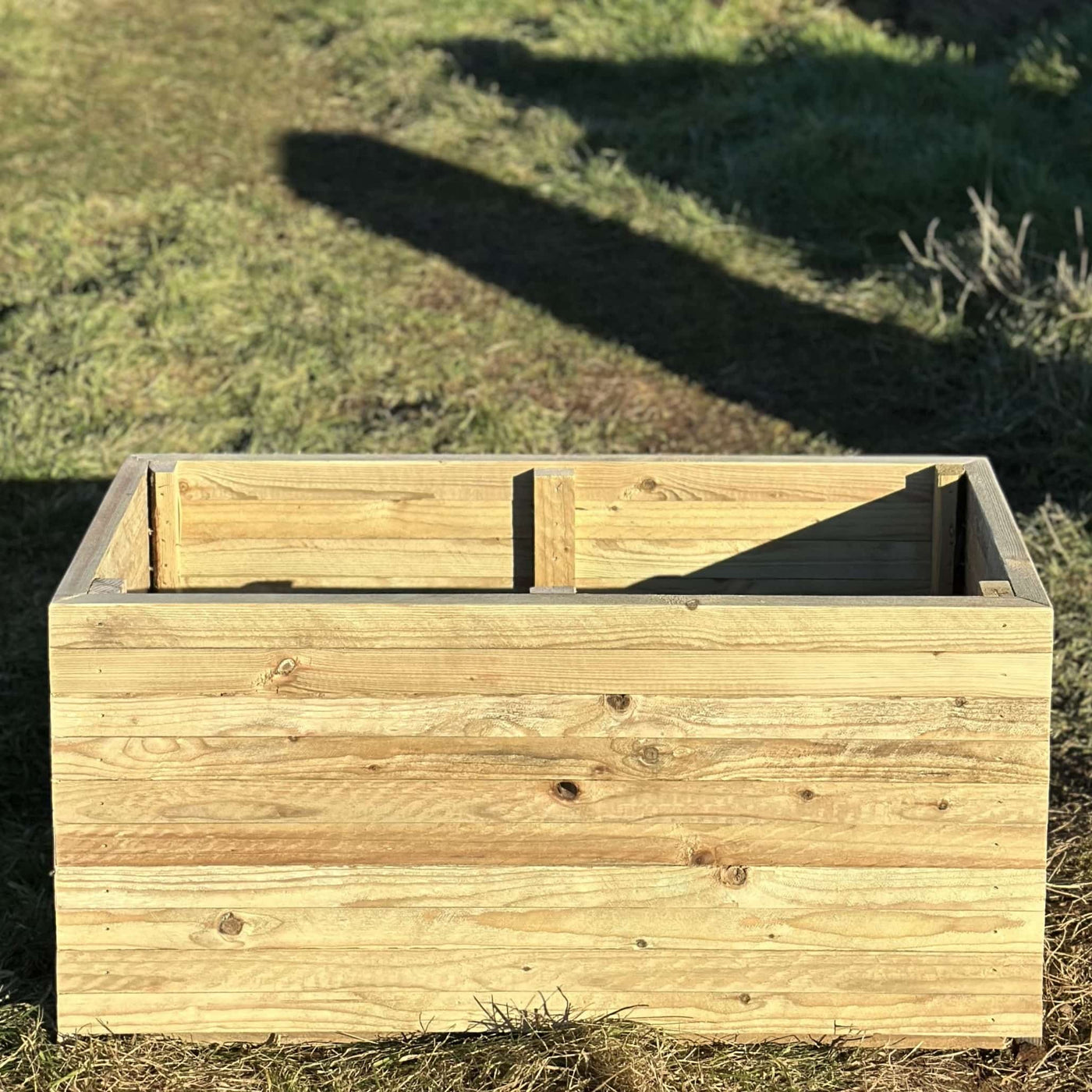 Rustic slatted wooden planter, a view of the front and top. The planter is empty and placed in a sunny garden.