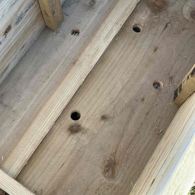 Inside view of drainage holes of a rustic wooden garden planter.