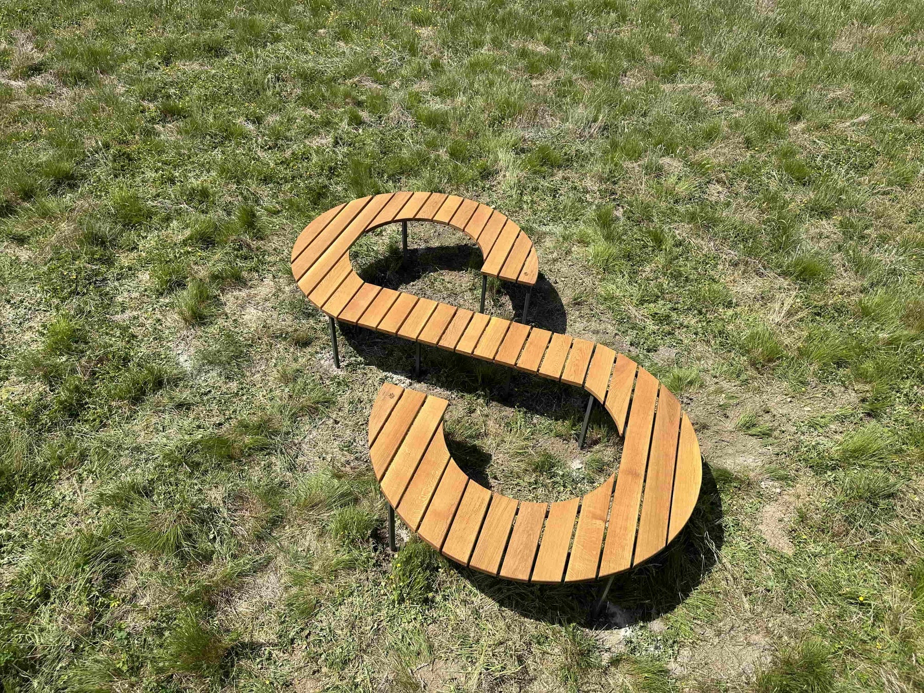 A large slatted wooden bench with an infinity S shape design, built for the woodland trust.