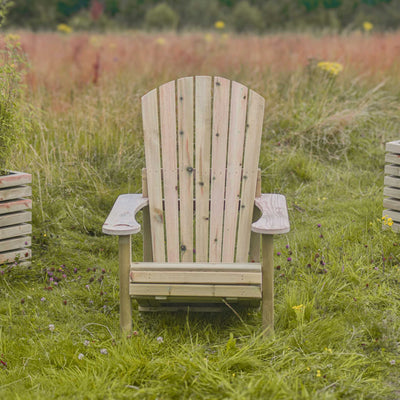 A wooden Adirondack Reclining Garden Chair with a hidden foot extension is shown on a lush garden lawn to highlight its sustainable timber construction and outdoor comfort—the front view of the chair is shown.