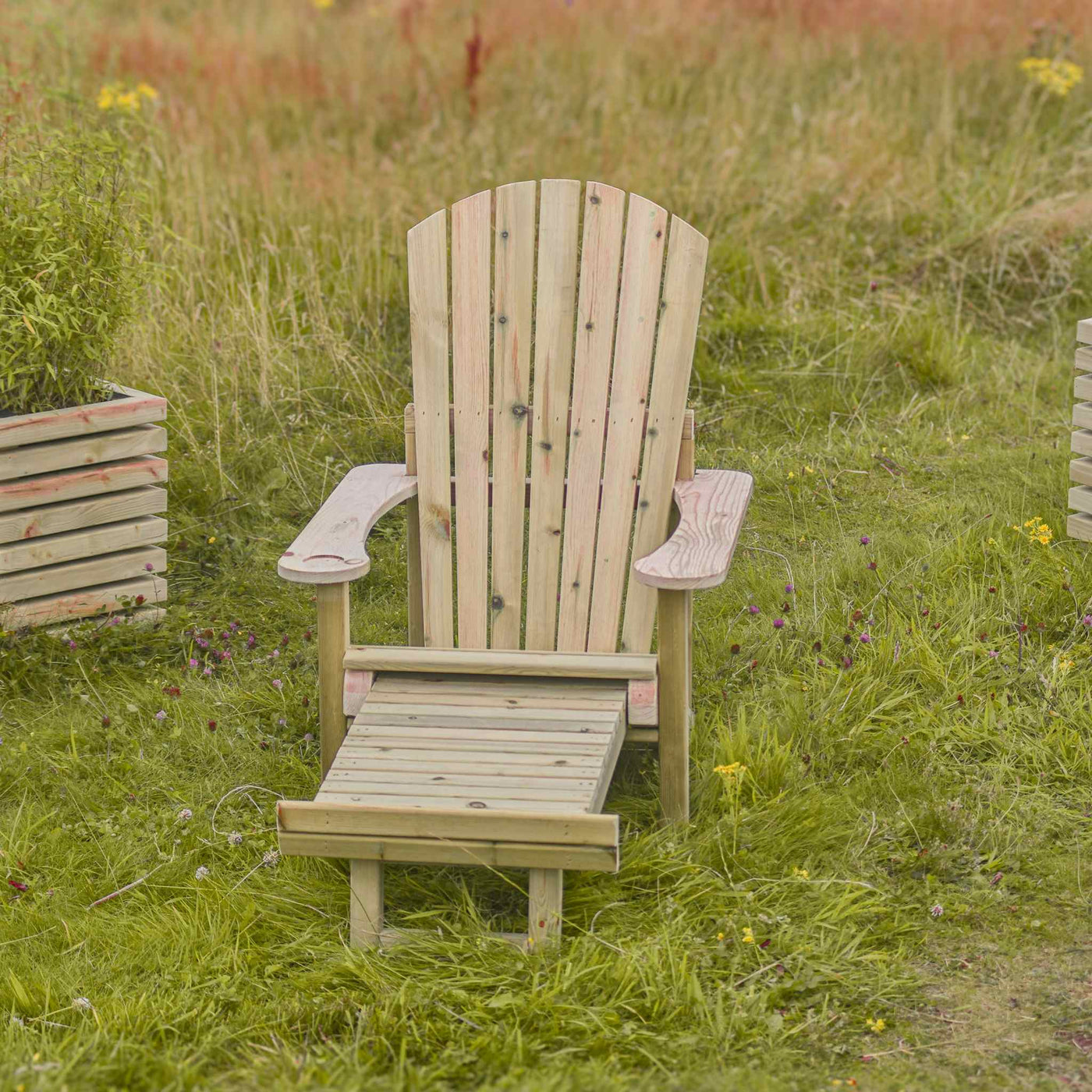 Wooden Adirondack Reclining Garden Chair on lush green garden lawn. The foot extension is shown. Made from FSC-timber and built for comfort.