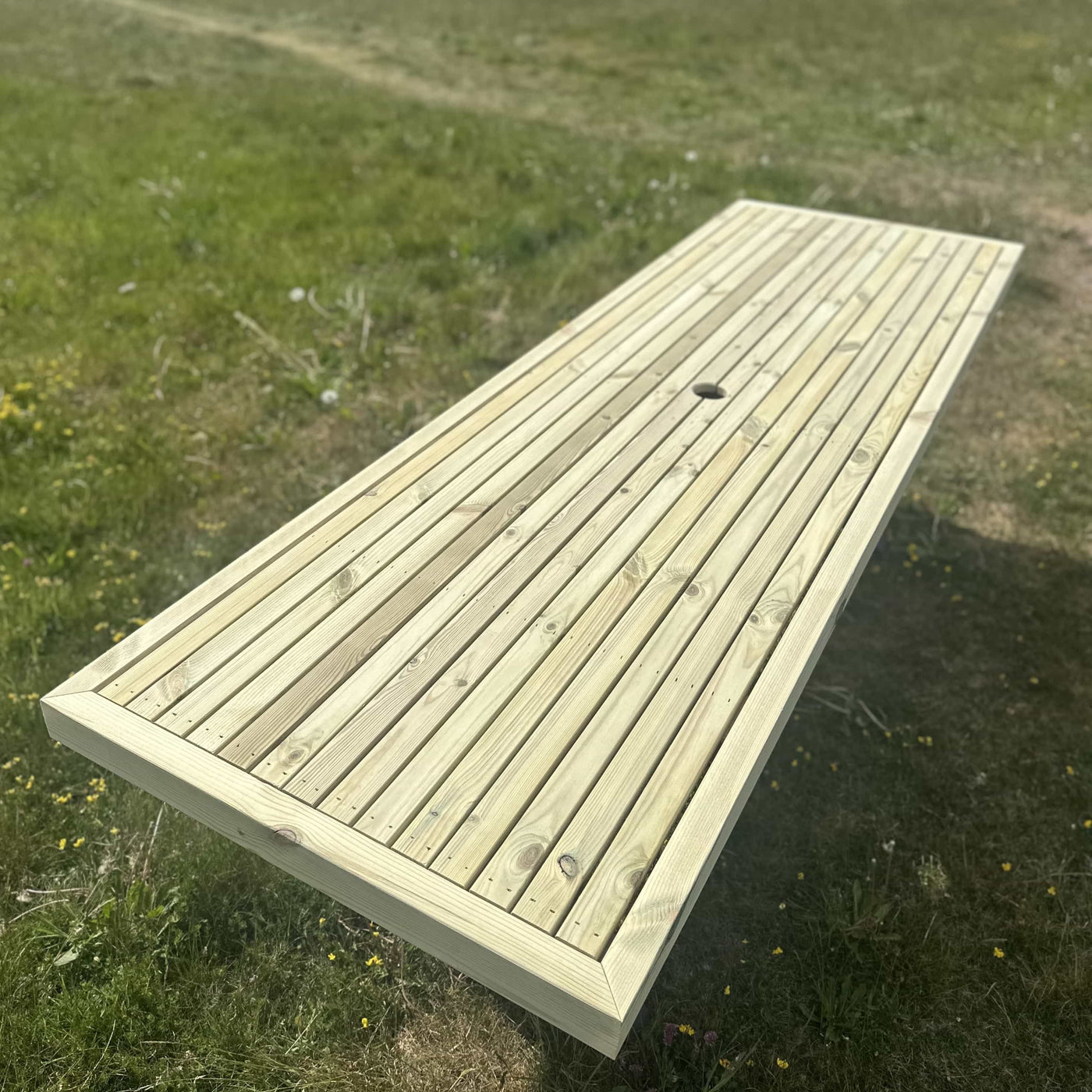 Wooden garden dining table with steel X legs and parasol hole, perfect for outdoor dining on sunny days.