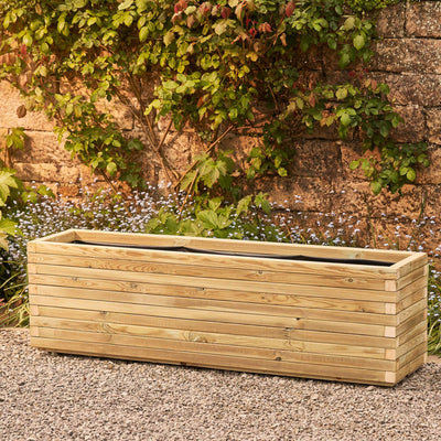 A XXL rectangular wooden garden planter, lined and ready for planting. The durable timber planter has a modern, sleek design and is placed in front of a brick wall and climbing plant.