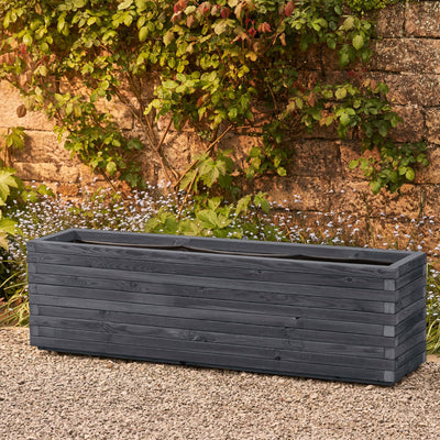 The XXL rectangular garden planter has an ironstone grey finish and is lined for added functionality. This durable wooden planter features a modern, sleek design and is placed against a wall with climbing green plants.