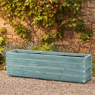 XXL rectangular garden planter in a beach hut blue finish, lined for added functionality. This durable wooden planter features a modern, sleek design and is placed against a wall with climbing green plants.