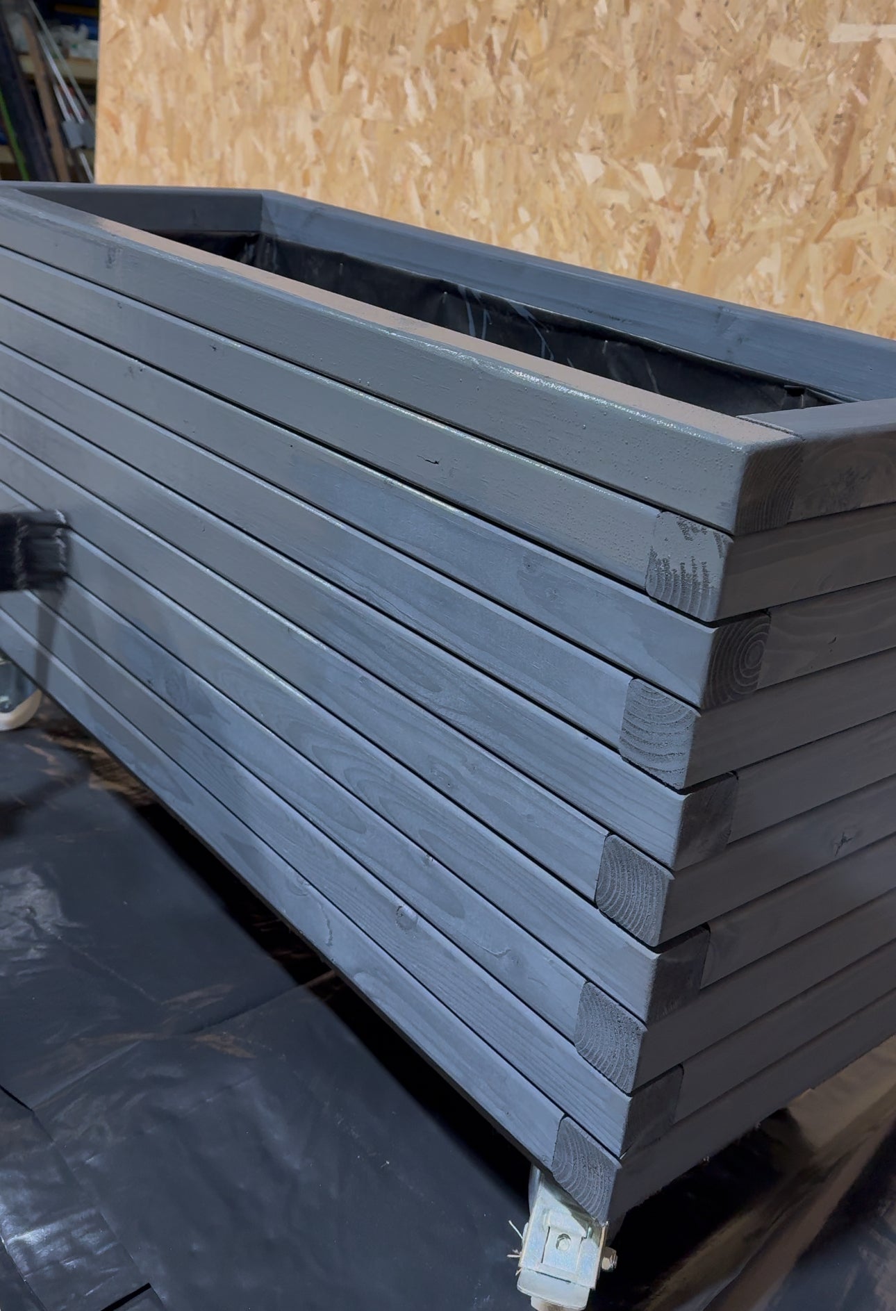 grey wooden garden planter on wheels in warehouse being restained with stain and paintbrush