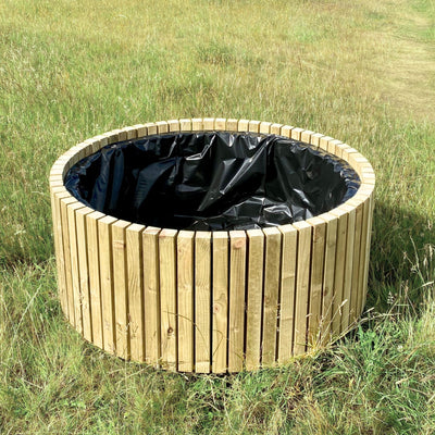 Wooden circular planter with black liner in a grassy field. Large round wood garden planter with lining, made from sustainable timber in the UK.