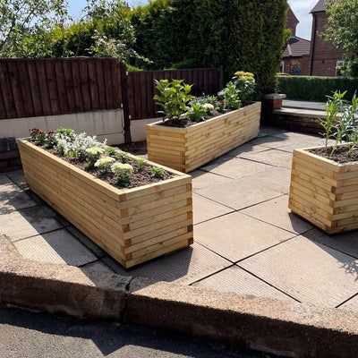 Three XXL Rectangular Garden Planters in a front garden full of soil and flowers. The durable wooden planters have a modern, sleek design.